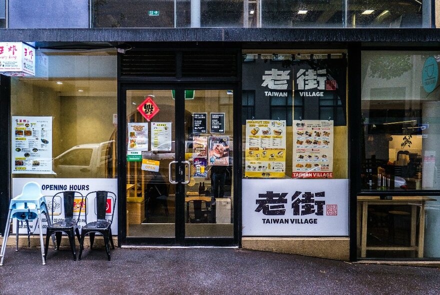 Street view of the exterior of Taiwan Village looking into the restaurant through the large glass windows, with menus and signage on display in the window.