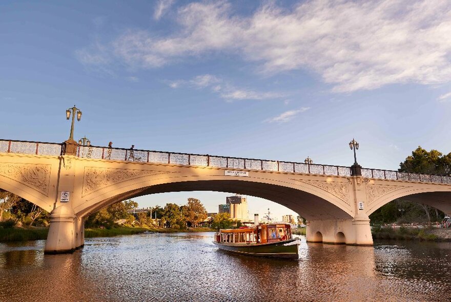 Boat travelling beneath a bridge on a river.