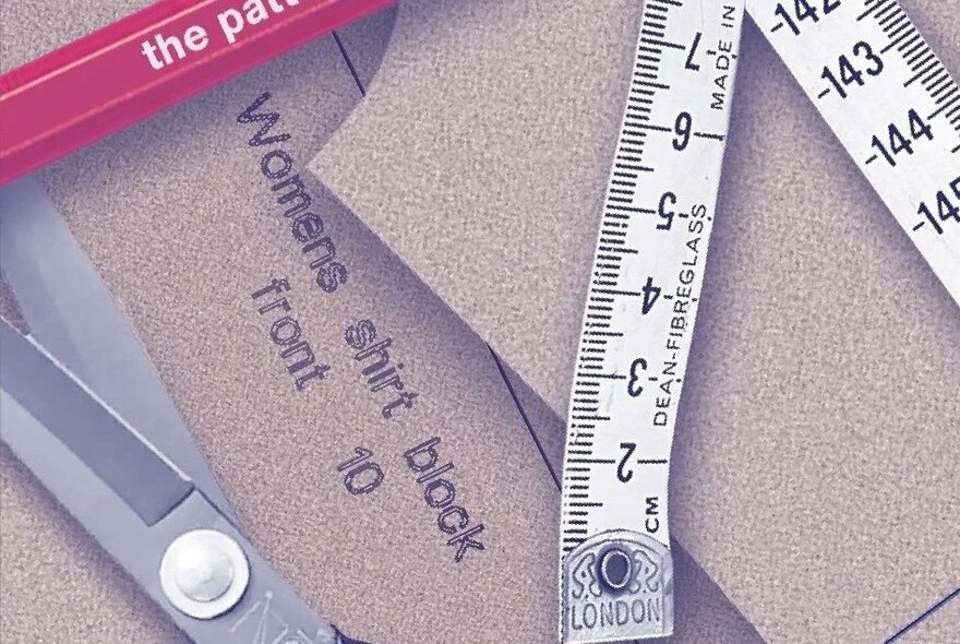 A sewing pattern for a women's shirt block, along with tailoring tools, including a measuring tape and scissors. 
