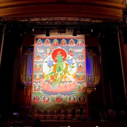 Large-scale Buddhist artwork on display in a theatrical setting with curtains.