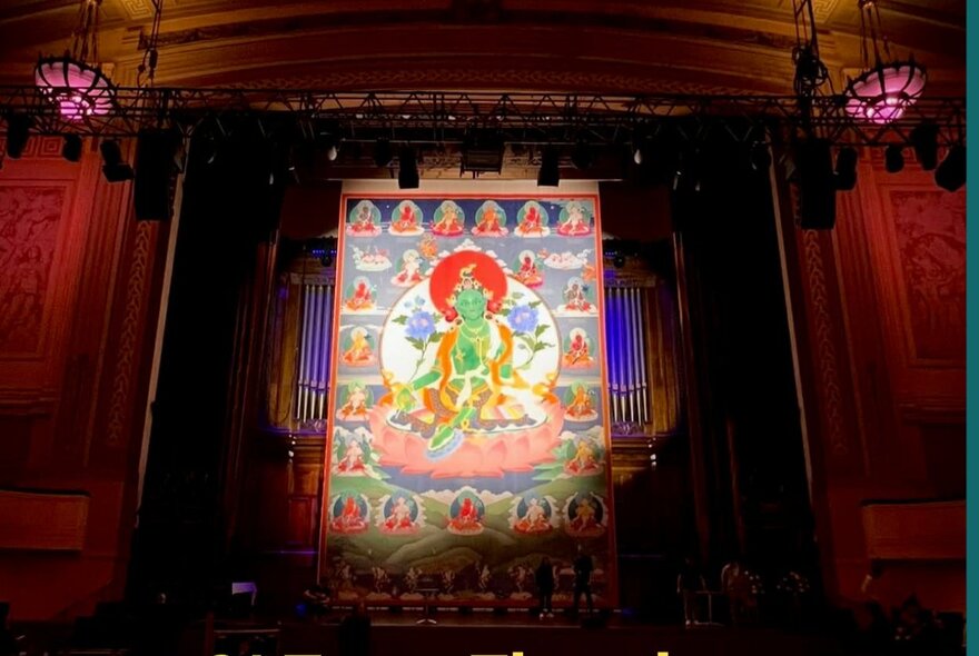 Large-scale Buddhist artwork on display in a theatrical setting with curtains.