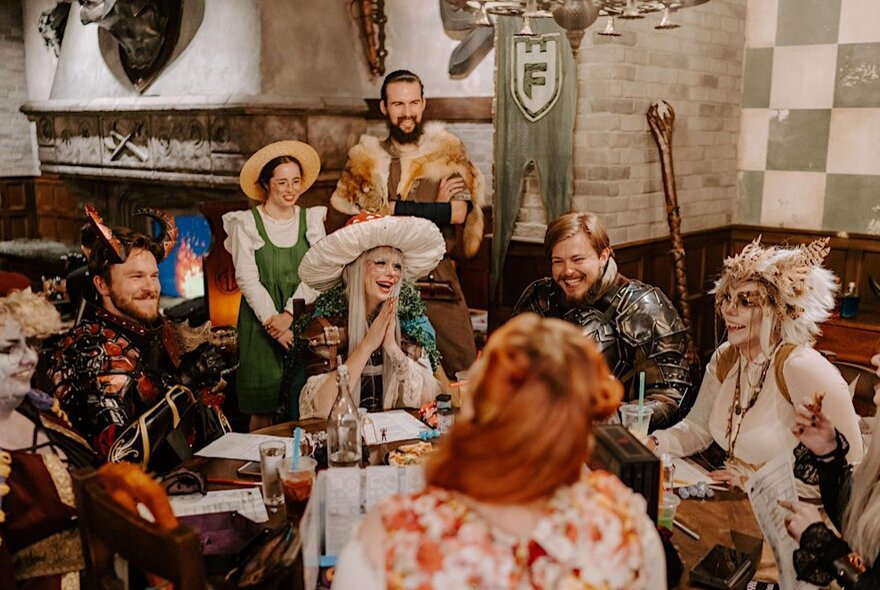 Gamers in cosplay dress seated around a table in a medieval-themed hall.