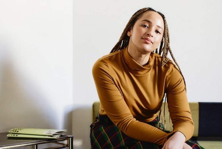 Woman with long dreads wearing a brown top in a lounge setting.