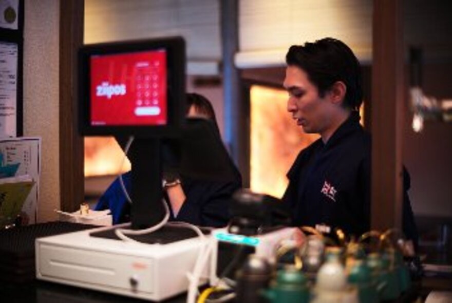 A waiter at a service counter inside a restaurant, intent on a task.