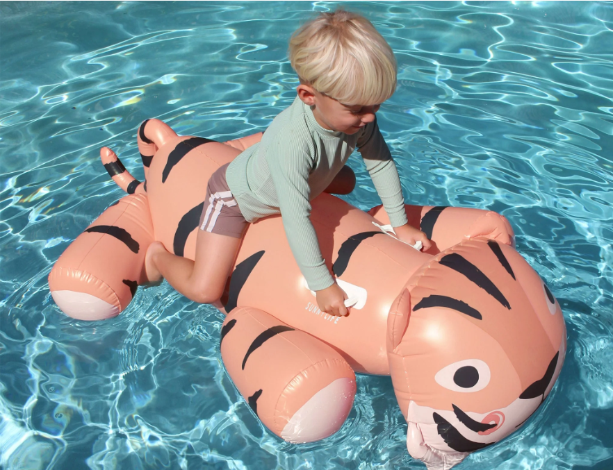 A child on a ride-on tiger floatie in a pool.