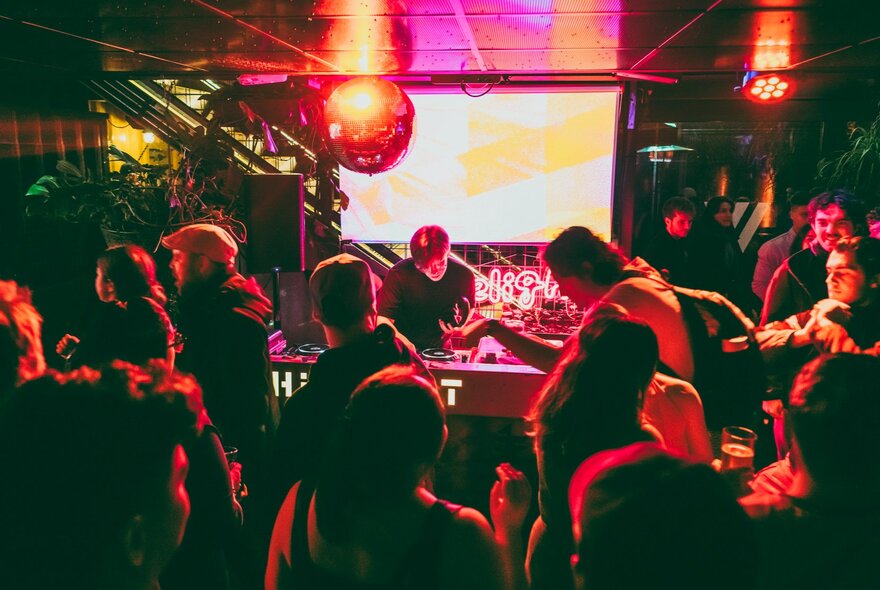 DJs at desk with crowd in the foreground under red lights.