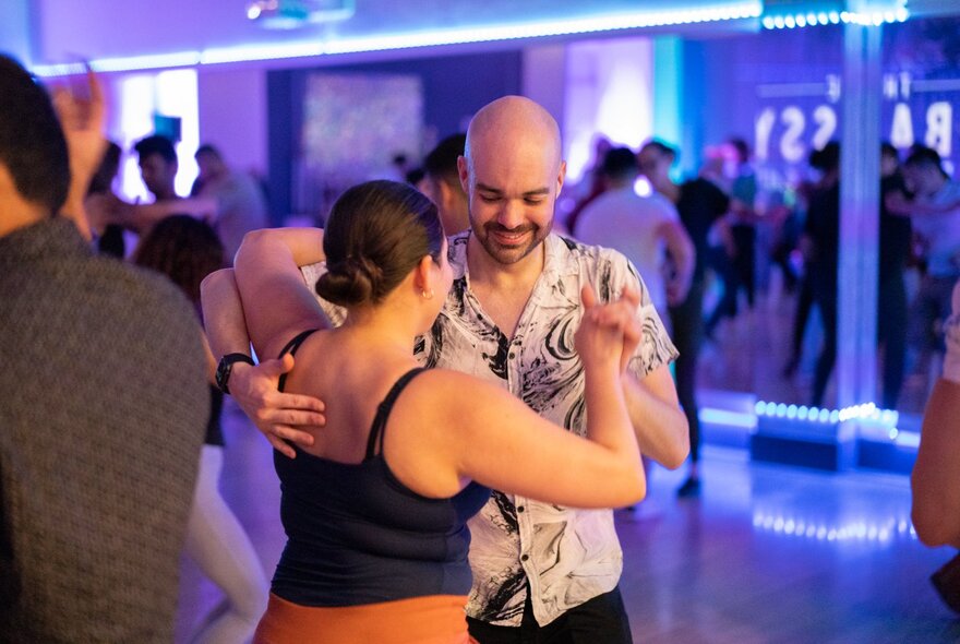A couple dancing with hands clasped on a dance floor with purple lights.