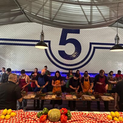 A group of people wearing aprons and standing behind a long wooden table as they participate in an Italian cooking class.