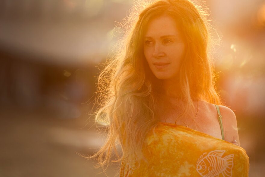 Warm-hued, blurred dappled image of a long-haired woman holding a wrap around her arm.