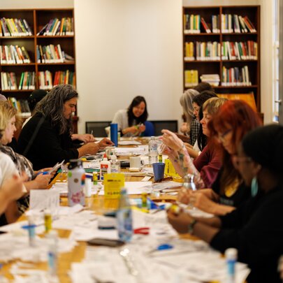 People completing craft work seated around a long table in a library setting.
