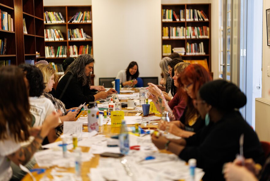 People completing craft work seated around a long table in a library setting.