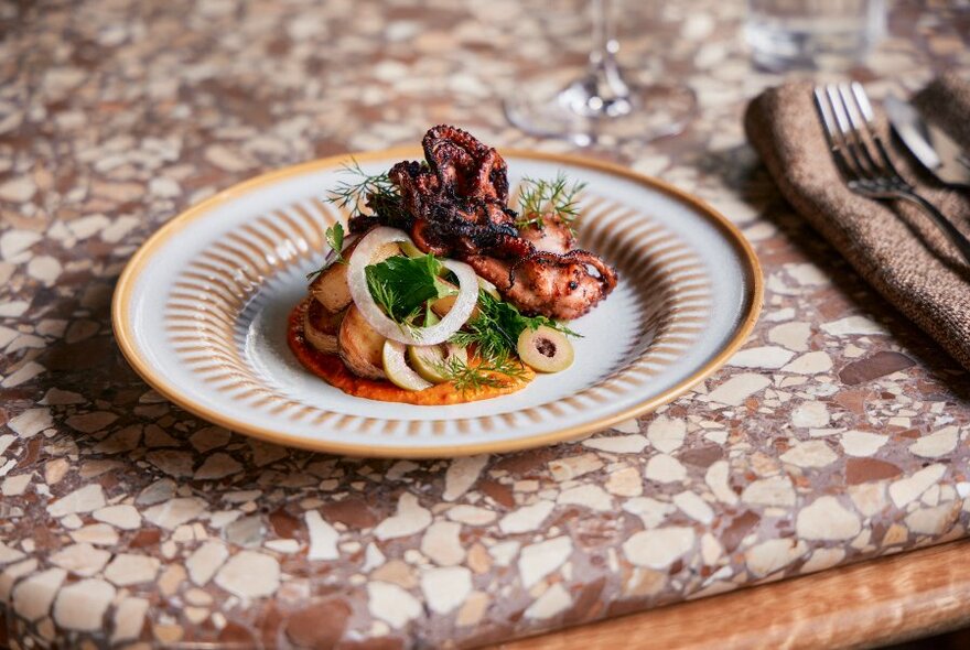 Plate of food on a terrazzo table top, with cutlery to the side.