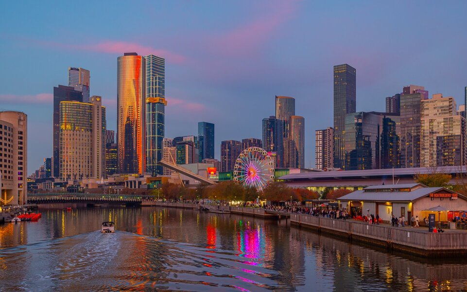 A Ferris wheel in the city at sunset with colourful reflections on the river.