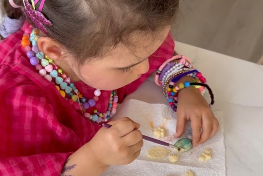 A young child painting white chocolated with edible paint.