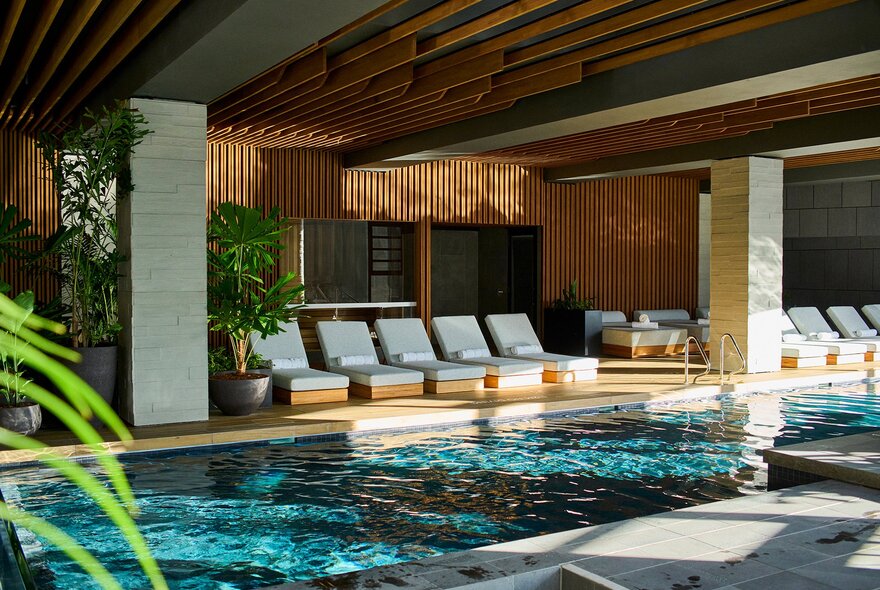 An indoor hotel pool with lounge chairs and plants.