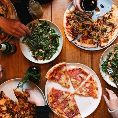Pizzas and salads on a table, with hands reaching out for slices.