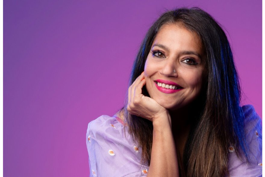 Woman with long dark hair, her hand resting on her chin.