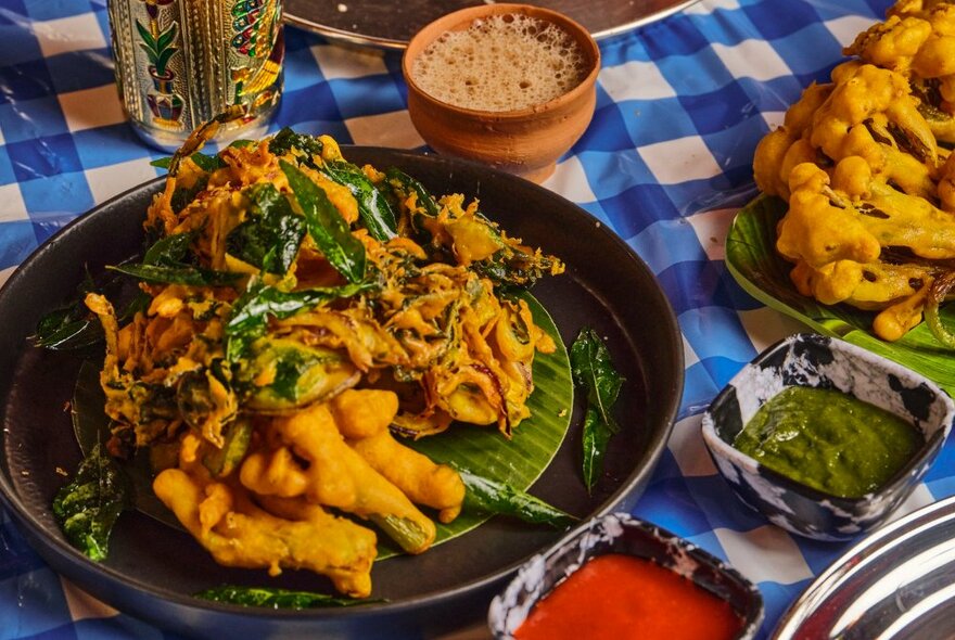 Traditional Indian fare on banana lead served on a table with a blue and white checked tablecloth.