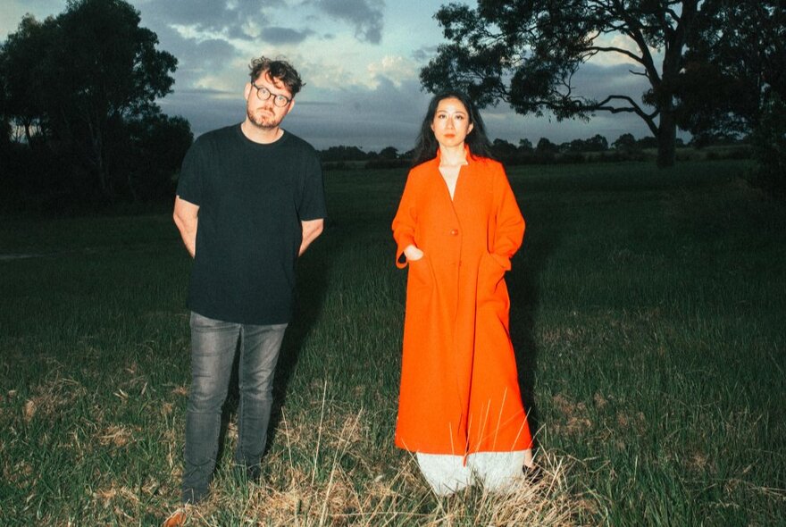 Musicians Mindy Meng Wang and Tim Shiel standing outdoors in a field in fading dusk light,