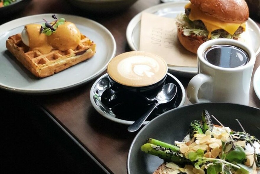 Table with an array of food including a waffle, a hamburger, salad and two cups of coffee.