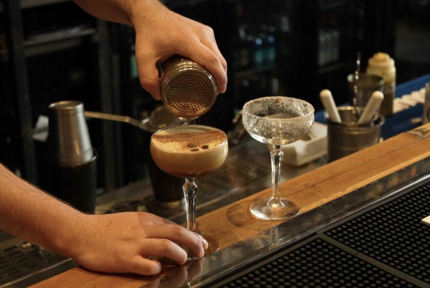 A bartender garnishing a cocktail on a bar counter.