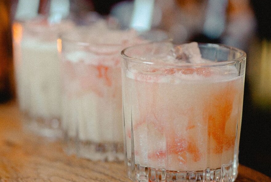 Three milky looking cocktails with orange syrup swirling through them. 