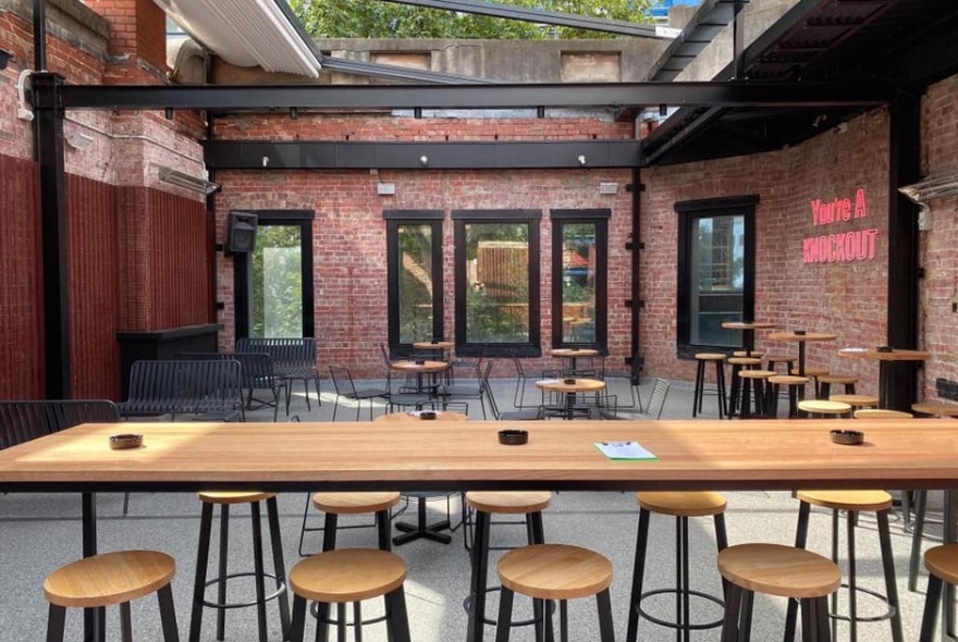 Long, wooden bench table with stools in a courtyard.