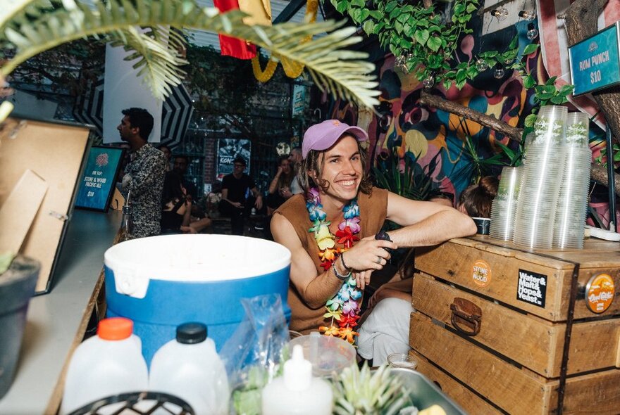 A smiling bartender at The Section 8 outdoor bar in front of juice bottles and a large blue tub. 