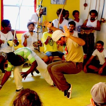 Two men dancing capoeira with onlookers sitting in a circle around them.