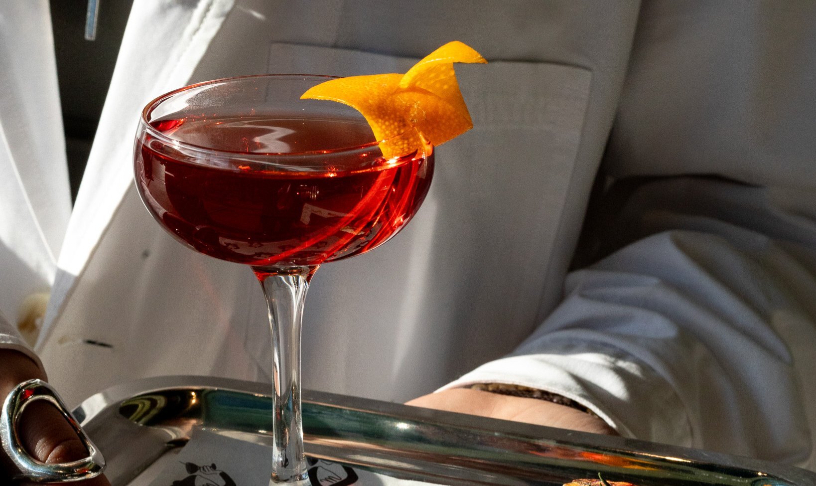A red cocktail with an orange twist on a silver tray.