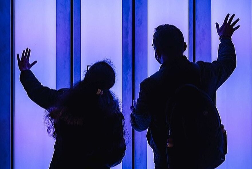Two people touching blue-lit pipes.