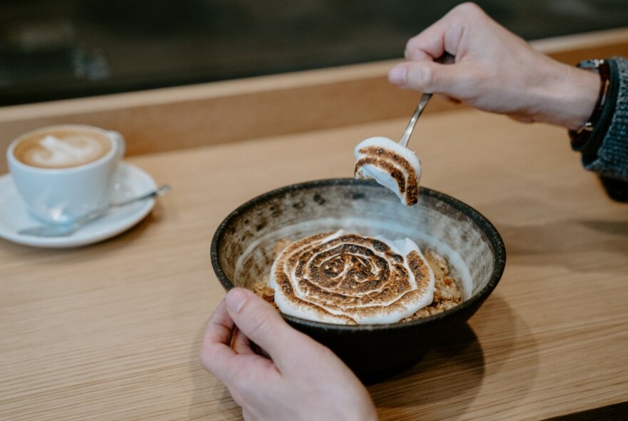 Hands tucking into a meal with a cup of coffee to the left.