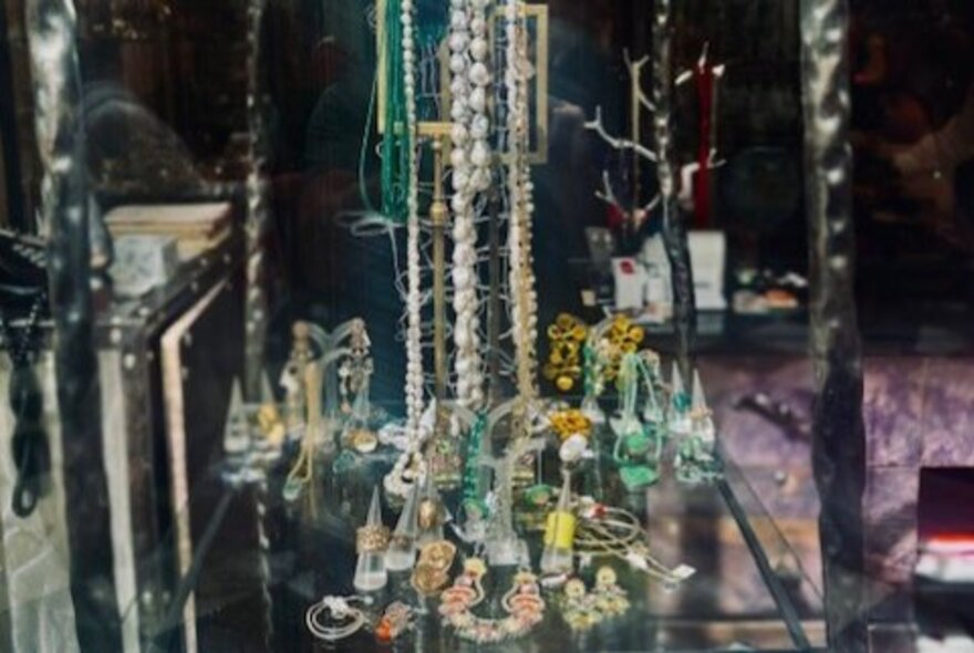 Costume jewelry, including long necklaces and earrings, displayed in a vintage shop window.