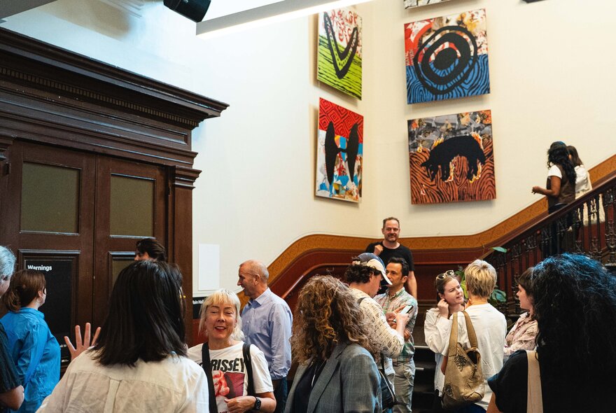 A group of people at the base of a staircase in an old building with artwork on the walls. 
