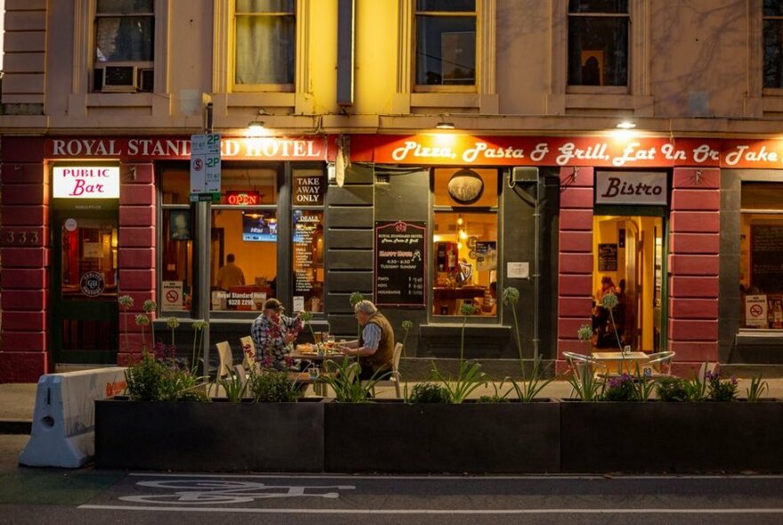 People seated outside the Royal Standard Hotel at night.