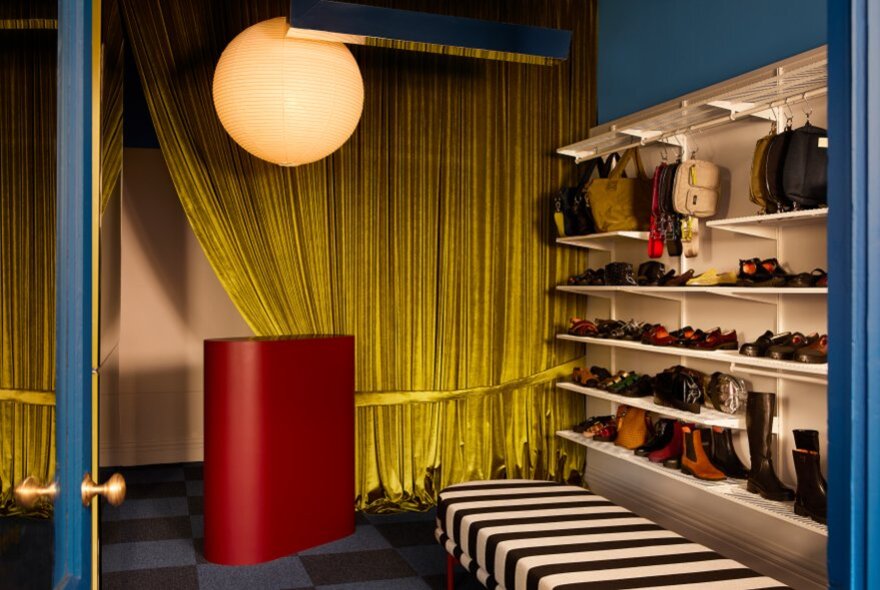 Shoeshop interior with striped seat and shoes on shelves, yellow curtains and paper globe light.