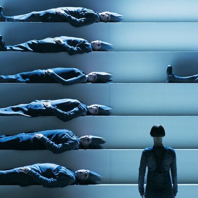 Abstract image in blue tones of a person looking at a staircase structure with a person laying on each stair. 