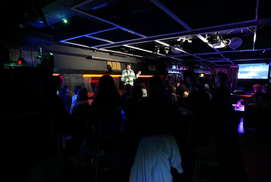 Performer on a stage in front of an audience in a dark venue.