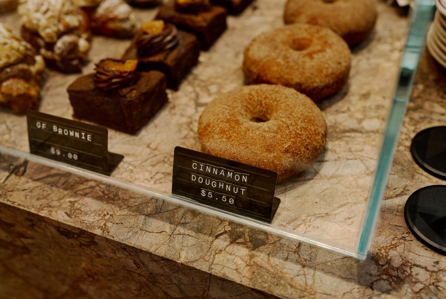 Rows of doughnuts and brownies behind glass on a marble counter.