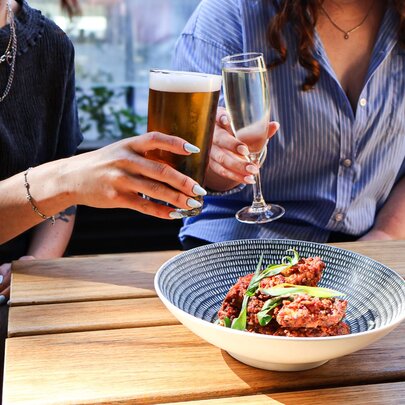 Two people (head unseen) clinking glasses over a bowl of food. 