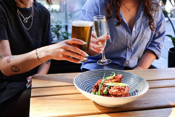 Two people (head unseen) clinking glasses over a bowl of food. 