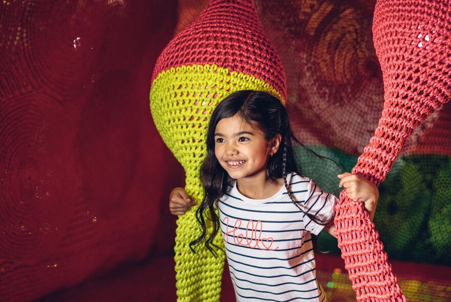 A young girl happily playing surrounded by large, colorful, textured structures.