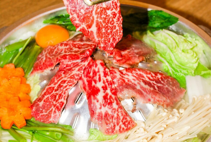 Wagyu beef slices on a silver tray with vegetables.