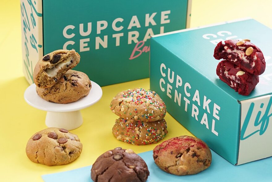 A selection of different cookies next to a takeaway green cardboard box with the words CUPCAKE CENTRAL written on the side.