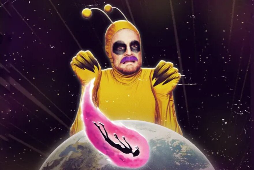 A performer in a yellow alien costume and face makeup hovering behind an image of the earth against a dark galaxy.