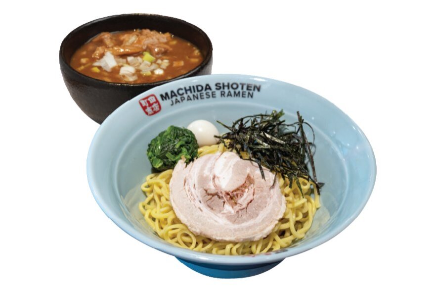 A white bowl of ramen from the Japanese chain Machida Shoten, with sliced pork and noodles in broth, with a smaller bowl of soup in the background.