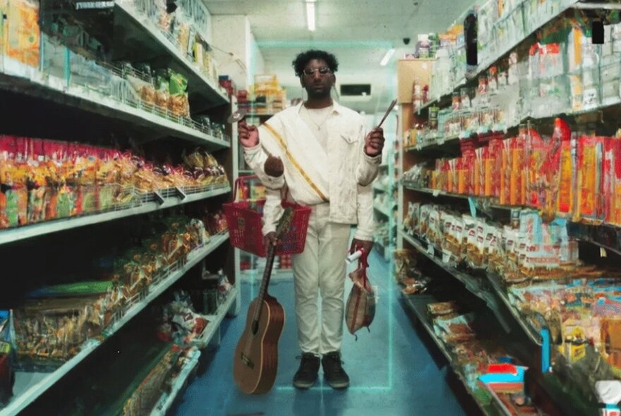 Person holding a guitar, standing in a supermarket aisle with a shopping basket.