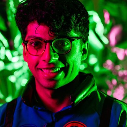 Comedian Rao lilt in red and green with floral backdrop.