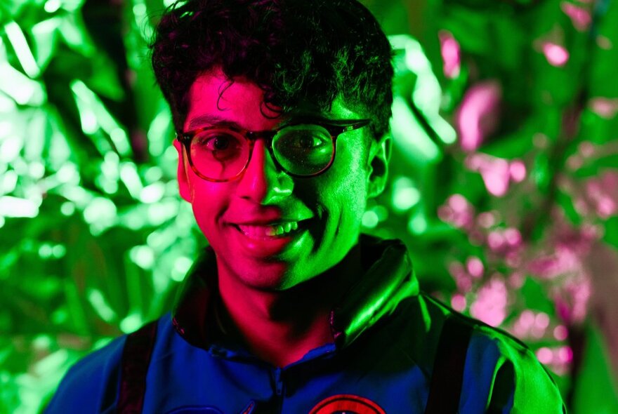 Comedian Rao lilt in red and green with floral backdrop.