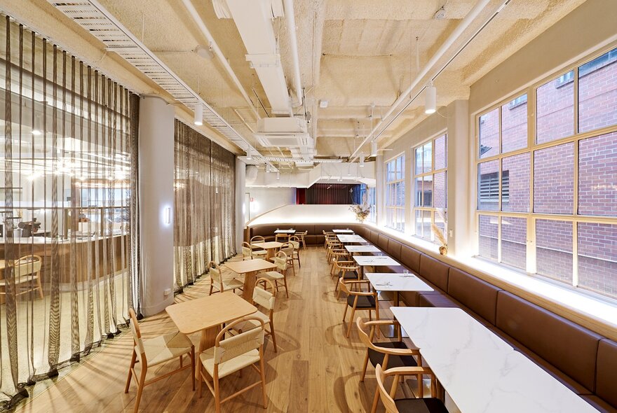 Light-filled interior of Soaz 22 cafe, with pale blonde wood tables and chairs, high ceilings, large windows and soft sheer curtains.